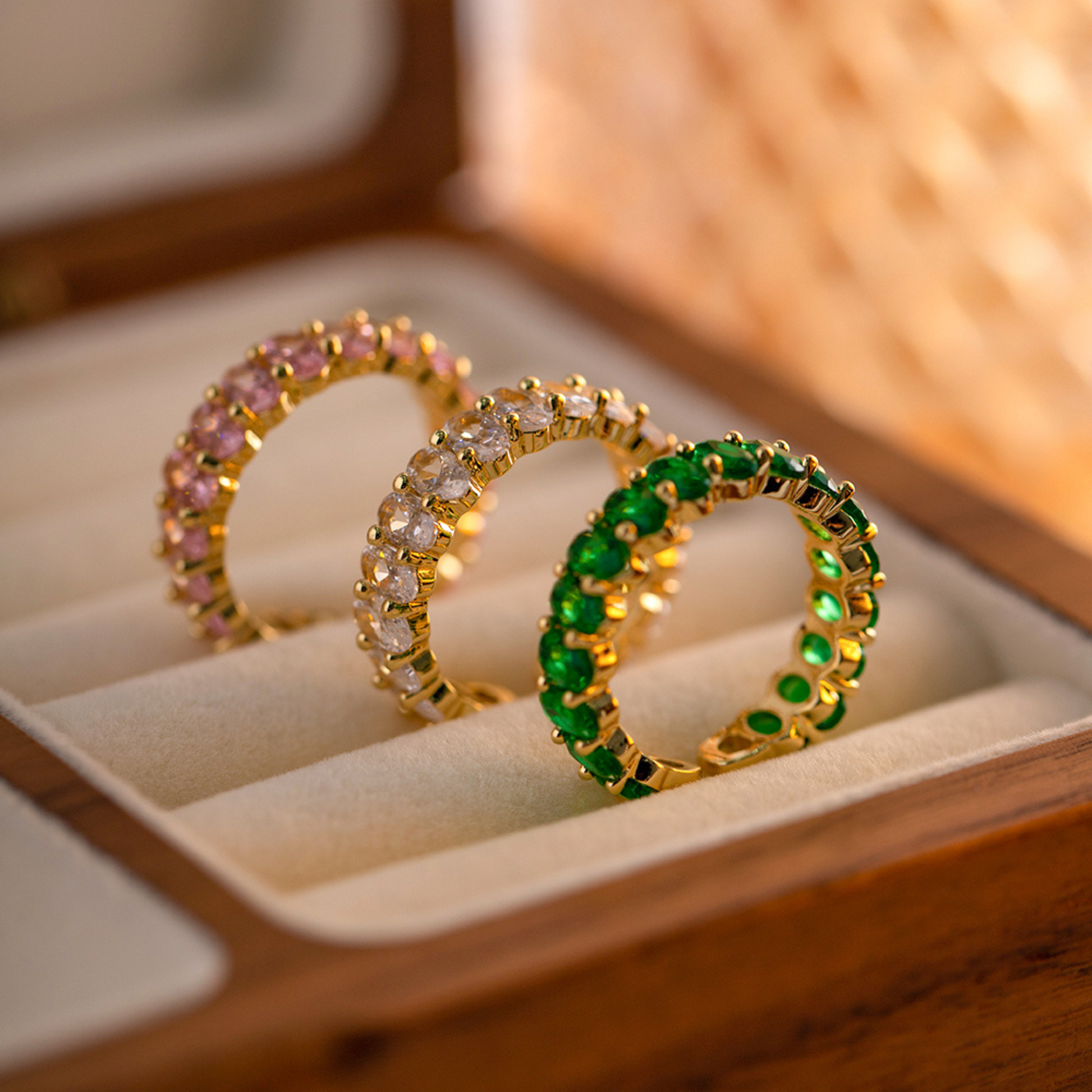 Drei 18K vergoldete Ringe mit funkelnden, grünen und rosafarbenen Cubic Zirkonia Steinen, präsentiert in einer eleganten Schmuckbox.