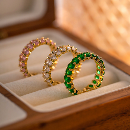 Drei 18K vergoldete Ringe mit funkelnden, grünen und rosafarbenen Cubic Zirkonia Steinen, präsentiert in einer eleganten Schmuckbox.