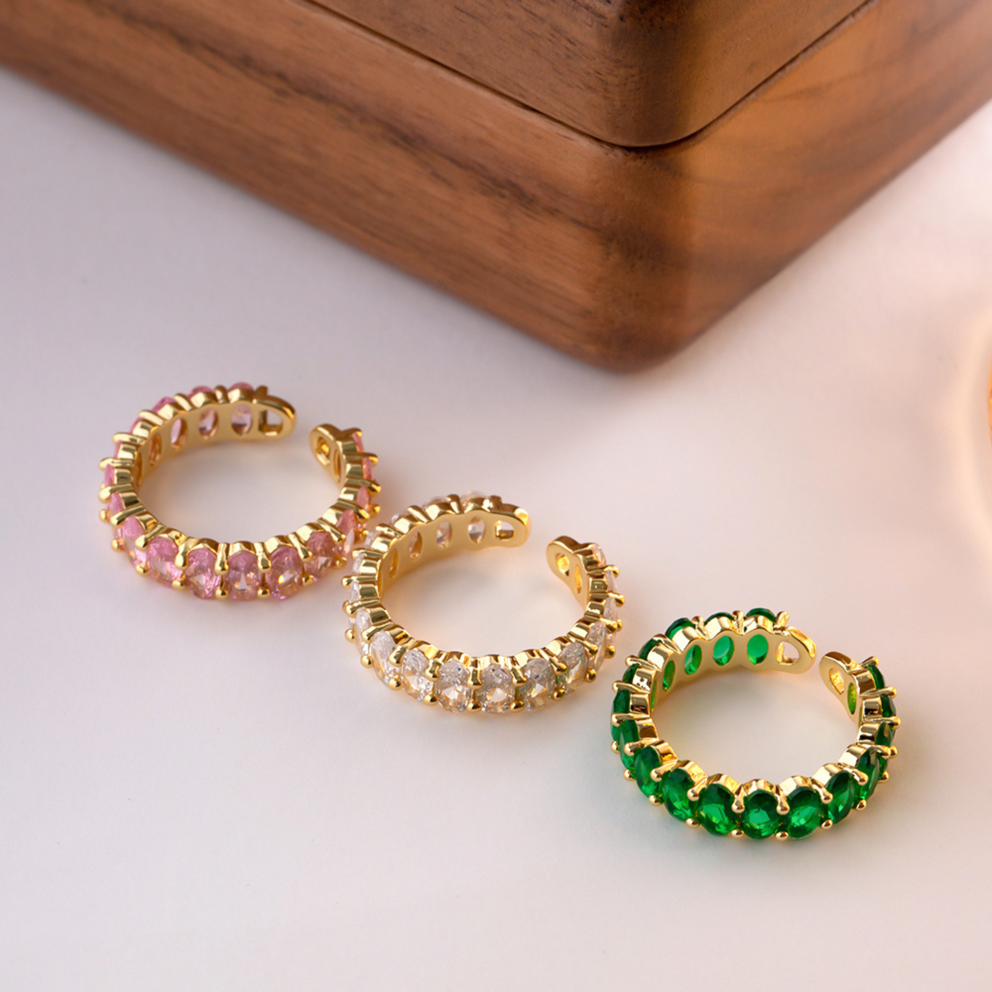 Drei 18K vergoldete Ringe mit grünen und rosafarbenen Cubic Zirkonia Steinen in einer Schmuckbox, die funkelnden Steine und die goldene Fassung betonen den luxuriösen Look.
